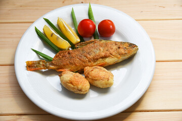 Fried fish on a plate with vegetables, lemon and onion