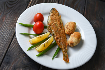 Fried fish on a plate with vegetables, lemon and onion