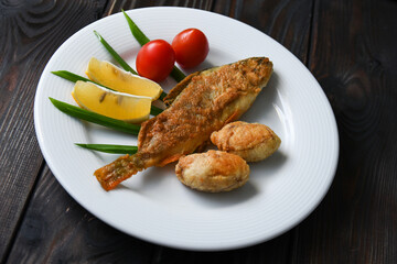 Fried fish on a plate with vegetables, lemon and onion