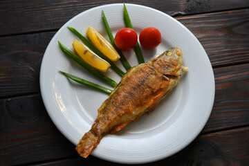 Fried fish on a plate with vegetables, lemon and onion