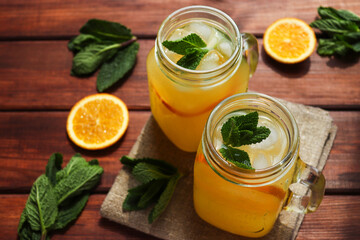 Fresh homemade citrus lemonade in jars with ice, mint and oranges on a wooden table. Summer refreshing drinks. Close-up, selective focus
