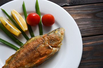 Fried fish on a plate with vegetables, lemon and onion