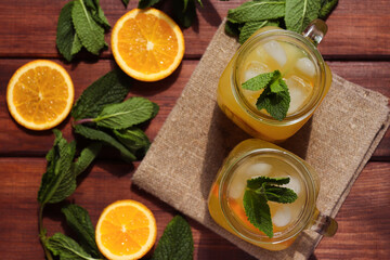 Fresh homemade citrus lemonade in jars with ice, mint and oranges on a wooden table. Summer refreshments. Close-up, selective focus, top view
