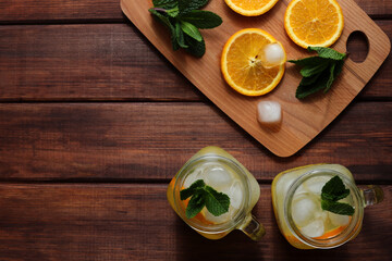 Fresh homemade citrus lemonade in jars with ice, mint and oranges on a wooden table. Summer refreshing drinks. Copy space, selective focus, top view