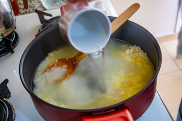 Adding boiled water to roasted rice in a pot