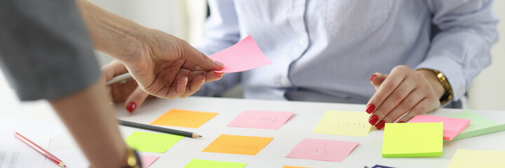 Woman giving pink sticker to colleague at table at workplace in office © megaflopp