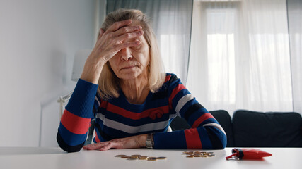 Worried old woman running out of money. Counting coins on the table. High quality photo