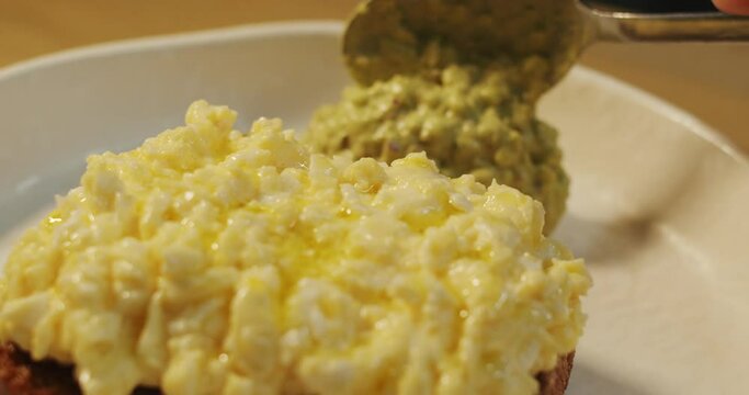 The chef spreads with a tablespoon freshly cooked guacamole on a plate with scramble eggs toast 
