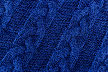 Closeup of the texture of a dark blue sweater. Wool jumper with braids useful as background. Detailed picture of the fabric of a pullover.
