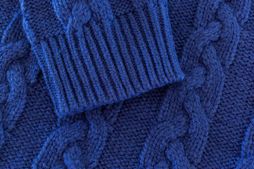 Closeup of the texture of a dark blue sweater. Wool jumper with braids useful as background. Detailed picture of the fabric of a pullover.