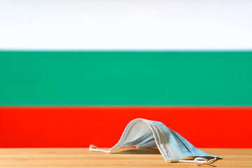 A medical mask lies on the table against the background of the flag of Bulgaria. The concept of a...