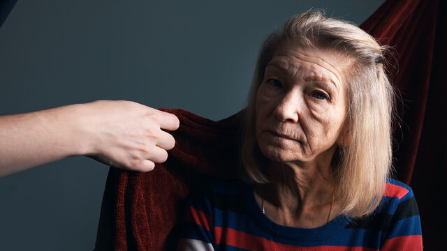 Young Person Covering His Grandmother With Red Blanket. Care Of Elderly People In Nursing Home. High Quality Photo