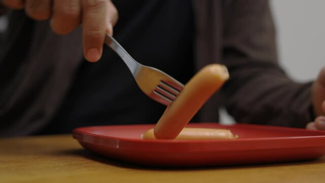 A young Asian man eating breakfast, he eats pork sausage. He poked it with a fork and bit his gut and chewed deliciously. Slow motion and movement short