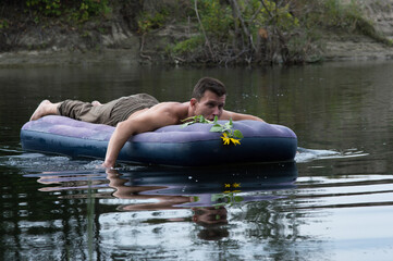 young man floats on an inflatable mattress on the river in summer