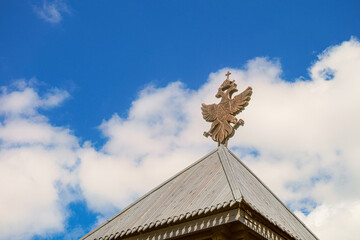 Obraz premium Wooden roof with historical coat of arms of the Russian Empire under blue sky. Ancient fortress roofing architecture.