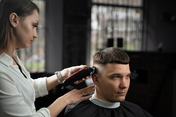 Woman barber making hairstyle in barbershop using clipper. Hairdresser cutting hair of handsome man.