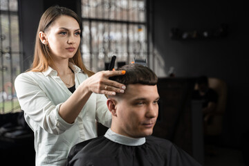 Woman barber making hairstyle in barbershop using clipper. Hairdresser cutting hair of handsome man.