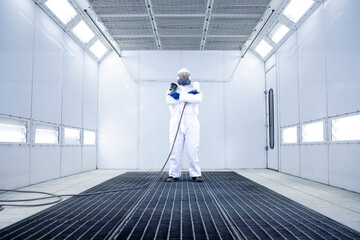 Portrait of car painter standing in paint chamber workshop holding painting gun.