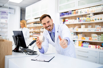 Pharmacist selling medicines in drug store and holding thumbs up.