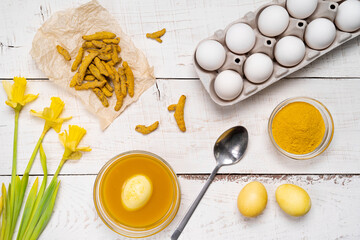 the process of painting Easter eggs with natural plant dyes, turmeric, on a white wooden...