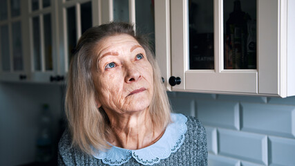 Sad lonely old gray haired woman looking through the window. Vulnerable person in quarantine. High...