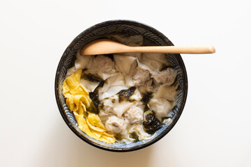 Top view of wonton soup with seaweed, egg, and dried shrimps in a ceramic bowl isolated on a white background.