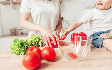 Son with mom are cutting vegetables on salad in kitchen and have a good time together. Happy family.