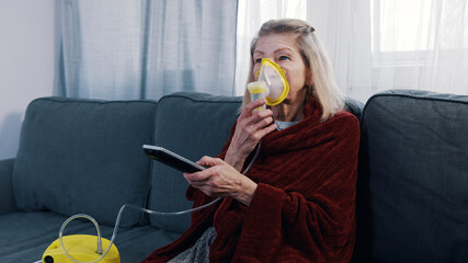 Elderly woman using oxygen mask while changing channels on tv at home. High quality photo