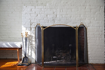 Fireplace with black fire guard screen and tools like shovel and poker. White brick wall