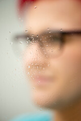 Frau mit roten Haaren und Brille, Nahaufnahme durch Fensterscheibe mit Wassertropfen, unscharfer Hintergrund