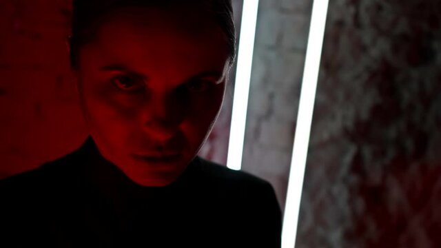 scary red light on face of adult woman in dark room, lady is looking at camera
