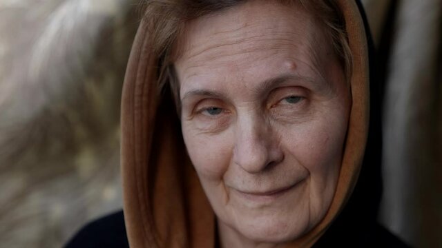 portrait of calm aged woman with wrinkled skin and head scarf, charming smile on face
