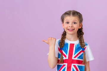 A little girl with pigtails and an image of the English flag on a T-shirt points her finger to the side.