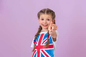 A little happy girl with pigtails and an image of the English flag on a T-shirt points her finger forward.
