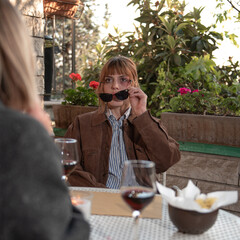 A woman sit down in a cafe with her friend, she is looking bruise’s friend. is holding sunglasses.