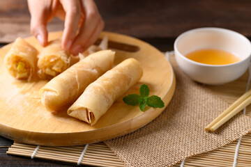 Asian deep fried spring roll stuffed with tofu and glass noodles on wooden board holding by hand and eating with chili sauce