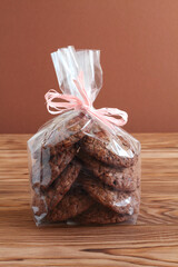 Сhocolate oatmeal cookies in transparent bag on a wooden table against a brown wall. Closeup. Macro