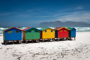 Naklejka premium Famous colorful beach houses in Muizenberg near Cape Town, South Africa with mountains of Cape of Good Hope Peninsula in the background.