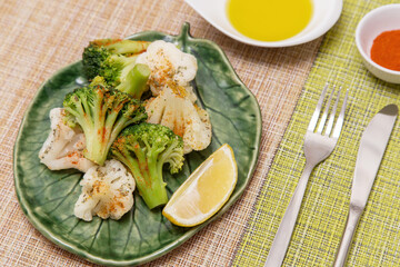 Broccoli and cauliflower with spices and lemon on green plate. Vegan vegetarian healthy diet food concept