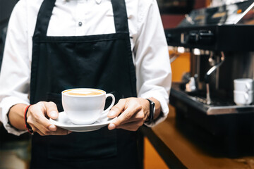 unrecognizable person working as a barista holding a cup of coffee.