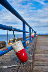 Red and white fender tied to blue metal rail at quai