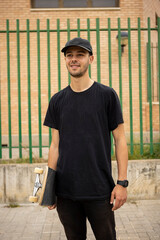 Young male in a black shirt and cap holding a skate in his hand on the street