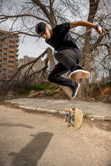 Young caucasian male in a black shirt and cap jumping with his skateboard