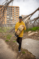 Young male in a yellow hoodie and cap holding a skateboard in his hands