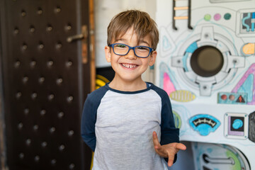 Portrait of happy caucasian boy with eyeglasses standing at home in room in day real people small male playful child looking to the camera smiling © Miljan Živković