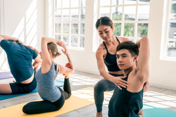 Asian female yoga instructor help and assist group of yoga student to make a good pose in white studio room with copy space. Concept of healthy lifestyle for fitness and yoga center.