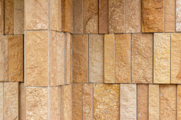 Corner angle view of a modern style rough textured limestone brick wall background with attractive vertical aligned natural kasota stone blocks in varying widths and shades of light brown.