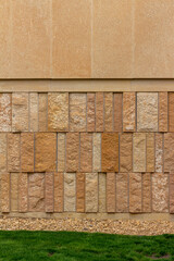 Modern style rough textured limestone brick wall with attractive vertical aligned natural kasota stone blocks in varying widths and shades of light brown, with foreground of grass and stone edging.