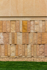 Modern style rough textured limestone brick wall with attractive vertical aligned natural kasota stone blocks in varying widths and shades of light brown, with foreground of grass and stone edging.