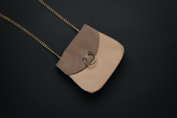 Beige leather women's bag with a chain strap on a black background. A fashionable women's accessory. Flat lay.